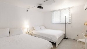A bedroom with two beds, a bedside table with a lamp, a window with blinds, and a ceiling-mounted projector. - Stylish Itaewon Getaway | Spacious Living, Projector, 4 Beds, 5 min to Station (Seoul)