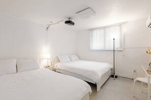 Een slaapkamer met twee bedden, een nachtkastje met lamp, een raam met zonwering en een aan het plafond gemonteerde projector.