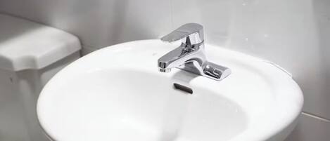 Une salle de bain avec un lavabo blanc, un robinet chromé et des toilettes.