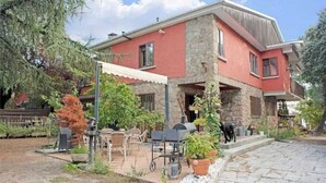 Una casa a due piani con facciata in pietra, un patio con mobili da esterno e un barbecue.