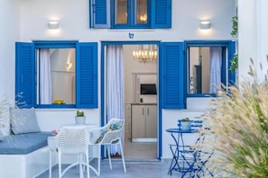 A hotel room with a balcony, a sofa, a dining table, and chairs. - Amore Villa (Santorini)
