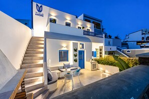 A modern villa with a staircase leading to a balcony, a reception area with a blue door, and outdoor seating. - Villa Amore (Santorini)