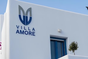 A building with a white facade and a blue door. The name 'VILLA AMORE' is displayed prominently. - Villa Amore (Santorini)