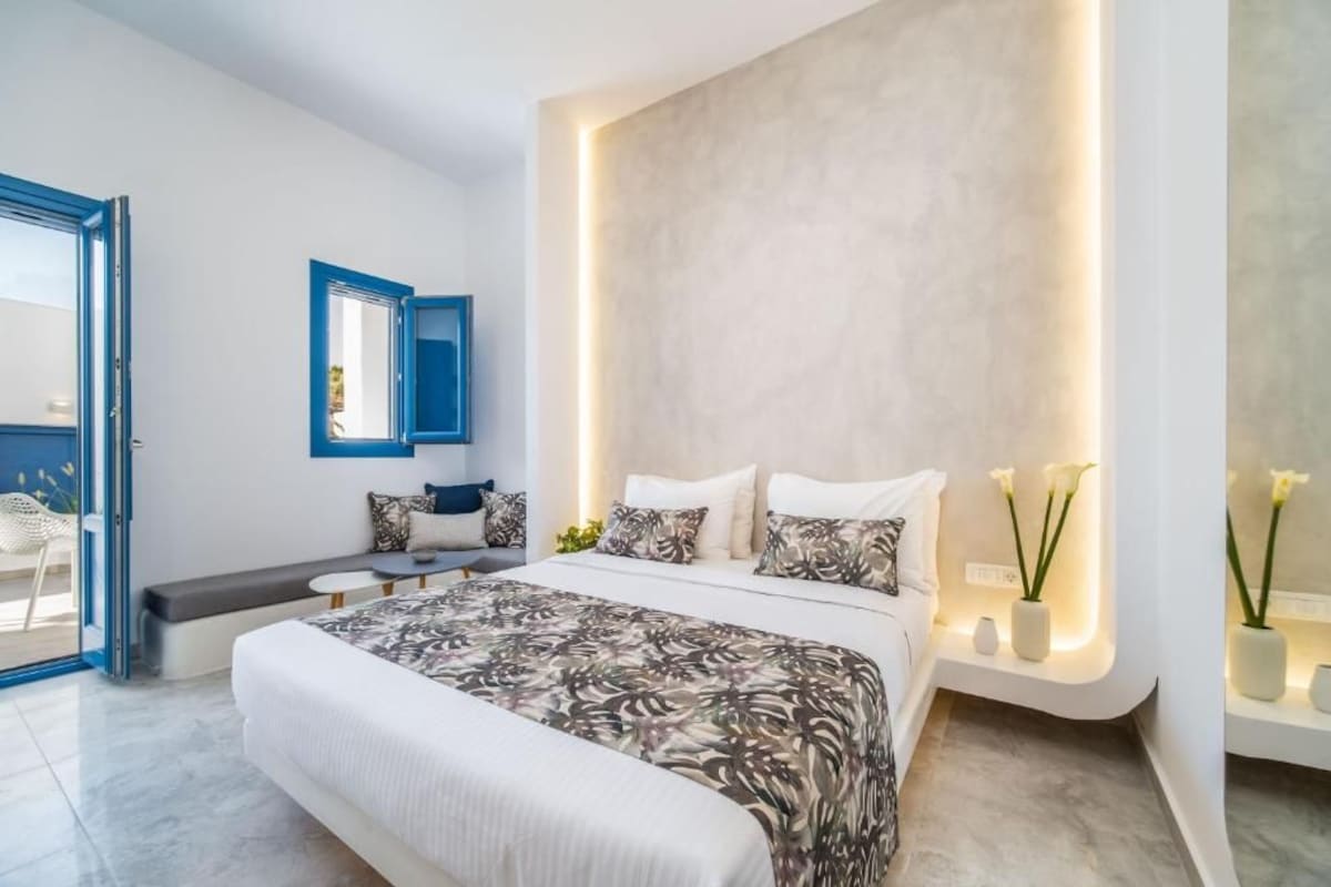 A modern bedroom with a large bed, bedside tables, a bench, and a wall-mounted mirror.