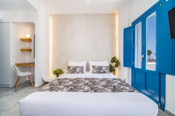 A bedroom with a bed, bedside tables, a desk, and a chair. - Villa Amore (Santorini)