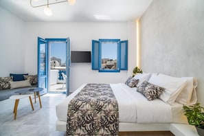 A modern bedroom with a bed, a sofa, a TV, and a balcony view. - Amore Villa (Santorini)