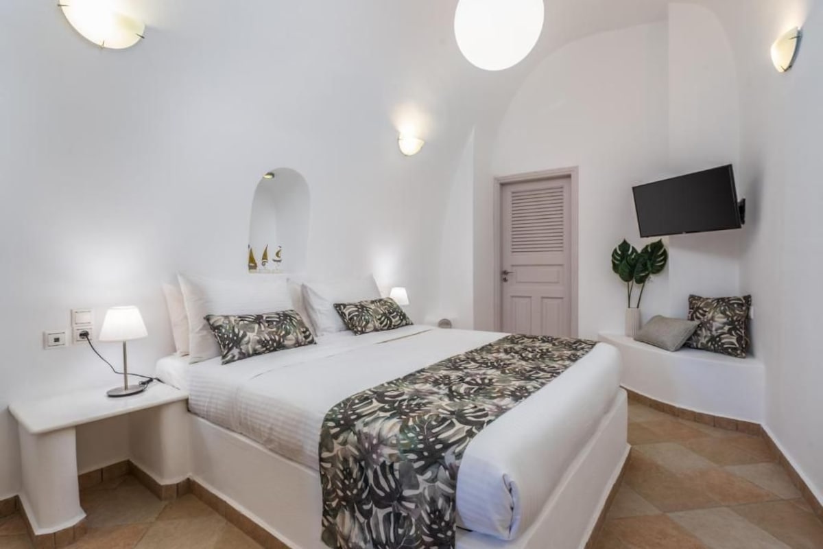 A bedroom with a bed, bedside tables, a flat-screen TV, and a door.