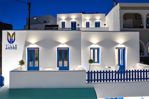 A white building with blue doors and windows, a sign reading 'Villa Amore,' and a pool area in the foreground. - Amore Villa (Santorini)