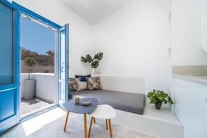 A compact living space with a balcony, a seating area with cushions, a small table, and a potted plant. - Villa Amore (Santorini)