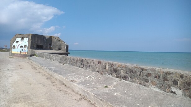 Ein Betongebäude mit Wandgemälde an einer Seite, gelegen an einem Strand mit klarem, blauem Wasser.