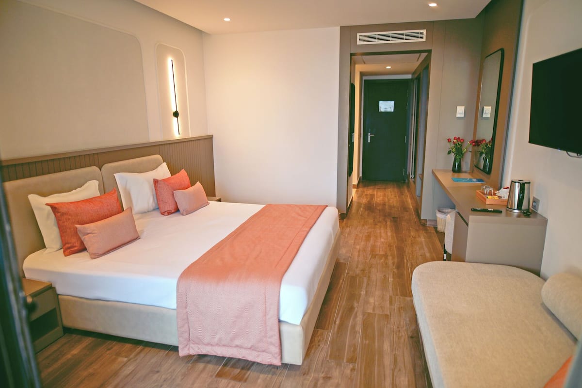 A hotel room with a large bed, bedside table, and a mirror.