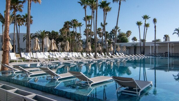 A poolside area with lounge chairs and umbrellas, surrounded by palm trees. - One Resort Premium  (Hammamet)