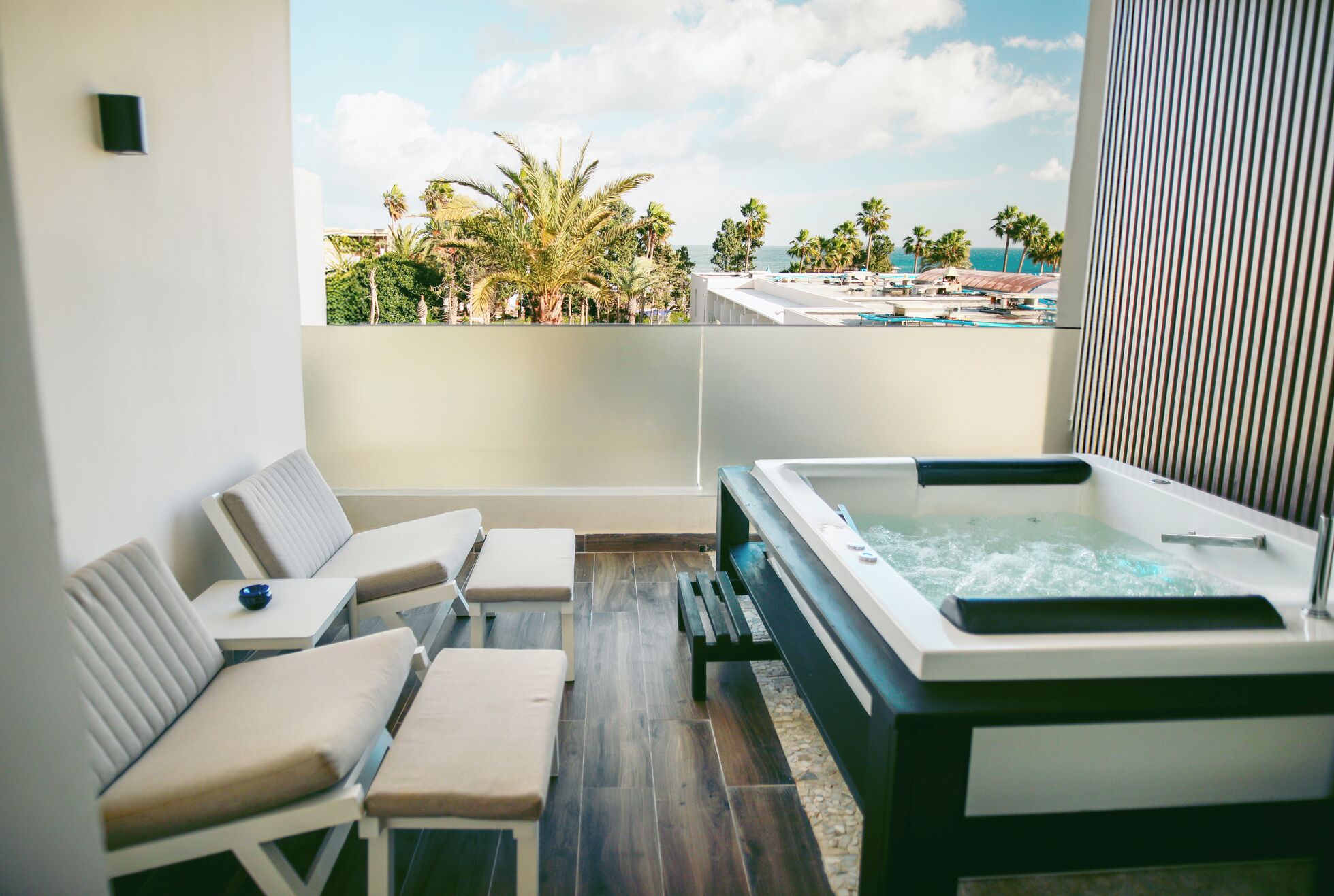 Un balcon doté d’un jacuzzi, de chaises longues et offrant une vue sur les palmiers et l’océan.