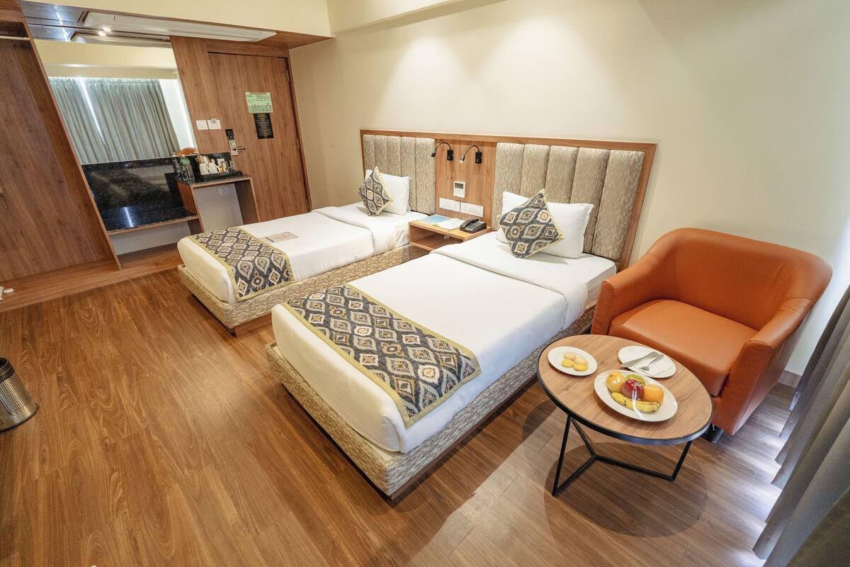 Habitación de hotel con dos camas, una mesita con fruta, una silla naranja y una kitchenette.
