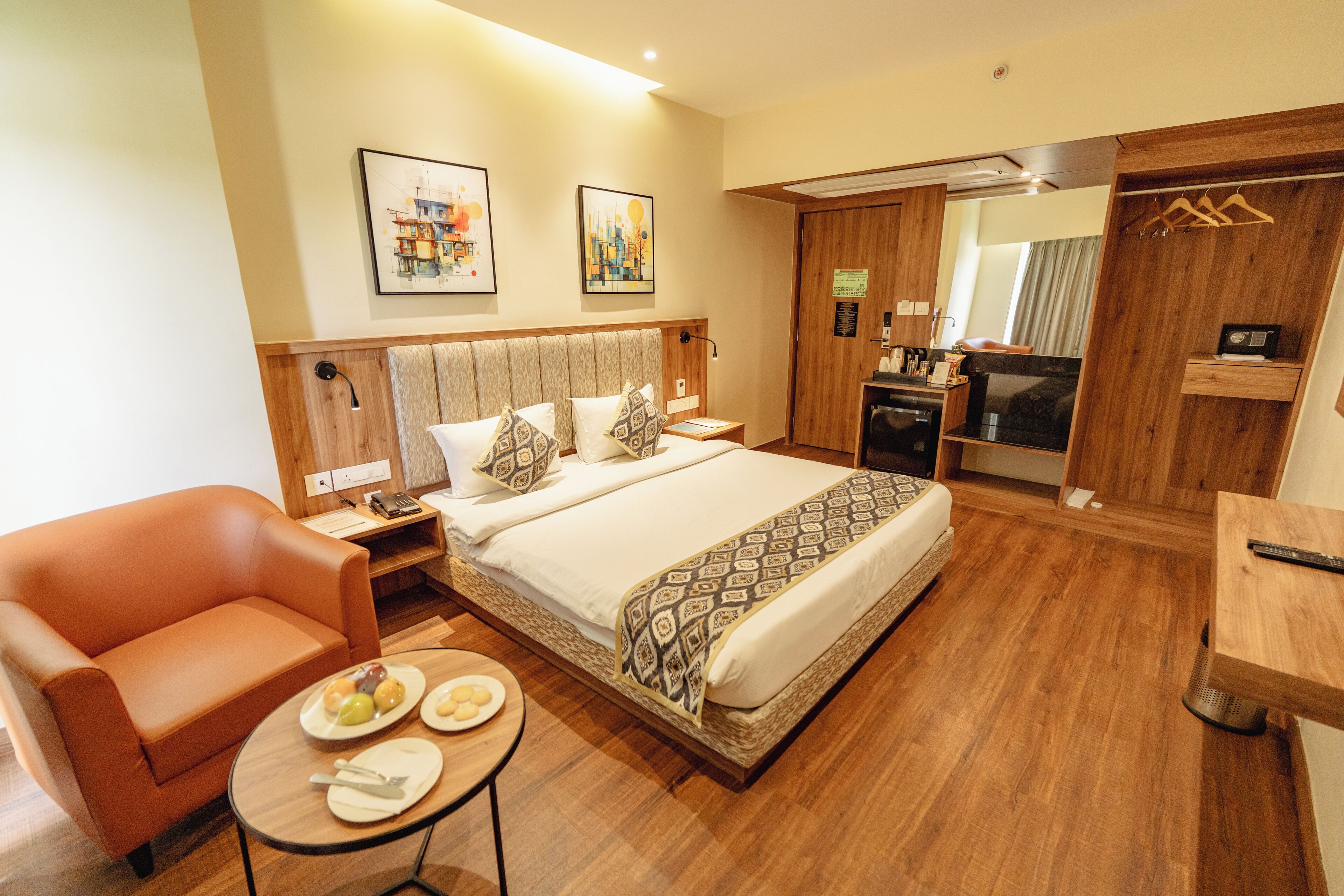 A hotel room with a bed, a sofa, a small table with plates, a TV, and a wooden cabinet.