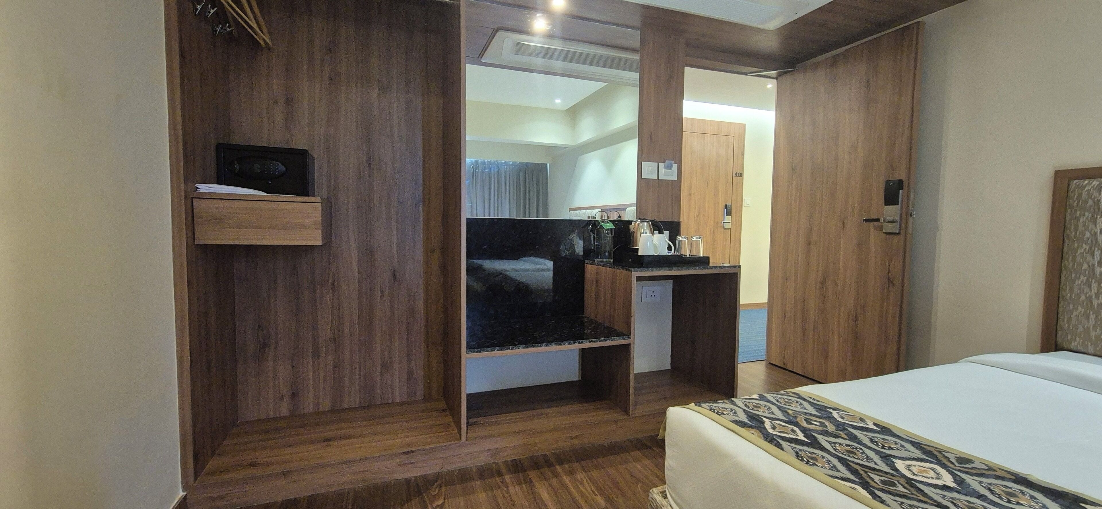 Una habitación de hotel con una cama, un armario de madera, un pequeño escritorio con cafetera y un espejo.