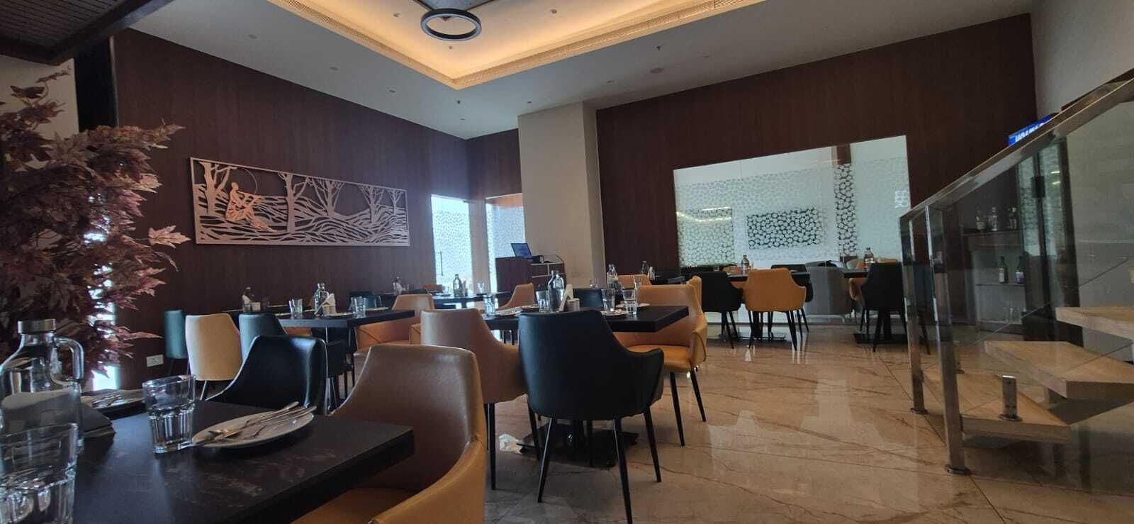 A modern dining area with multiple tables and chairs, a staircase, and decorative wall art.