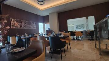 A modern dining area with multiple tables and chairs, a staircase, and decorative wall art.