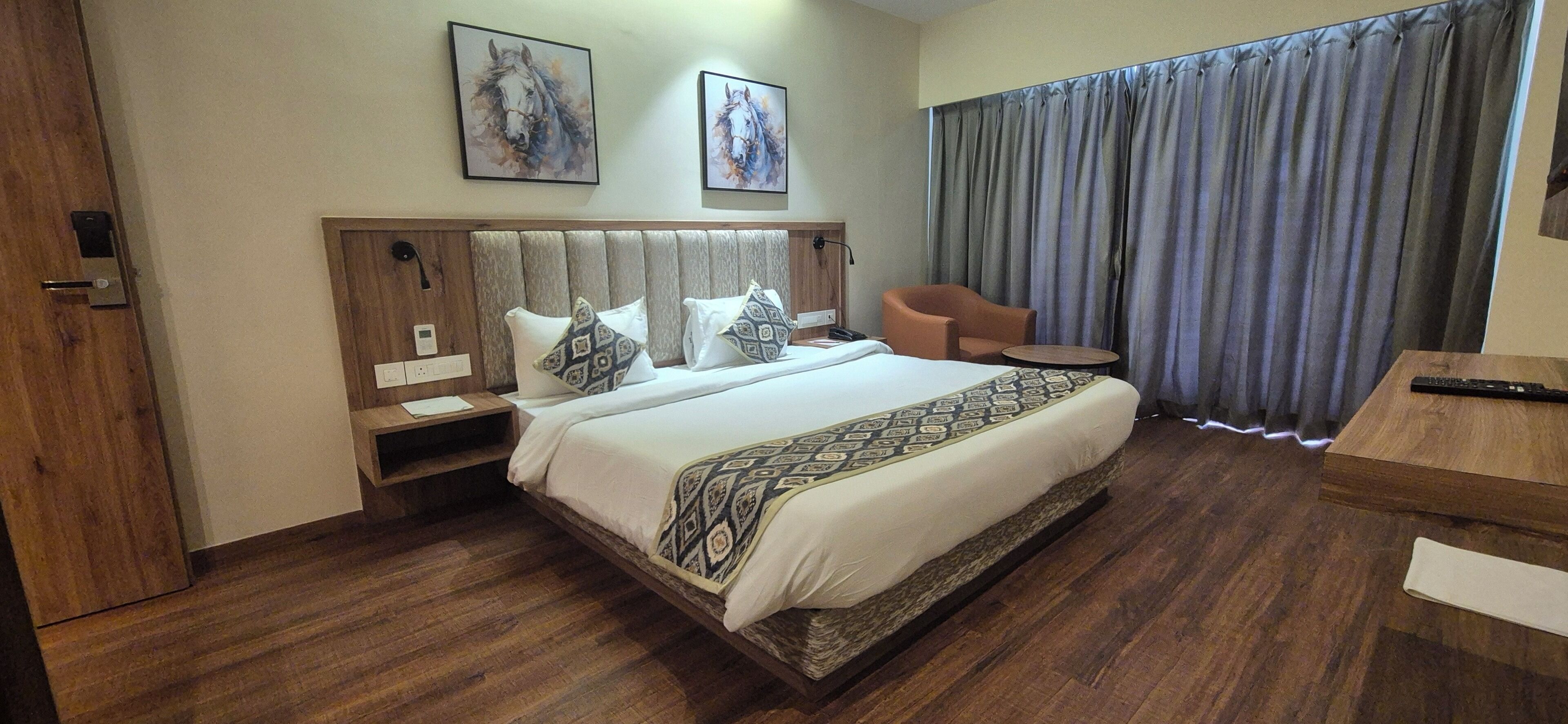Ein Hotelzimmer mit einem großen Bett, zwei Nachttischen, einem Sessel, einem kleinen runden Tisch und einem großen Fenster mit Vorhängen.