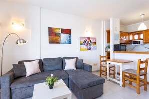 A modern living room with a grey sectional sofa, a white coffee table, and a dining area with wooden chairs and a white table.