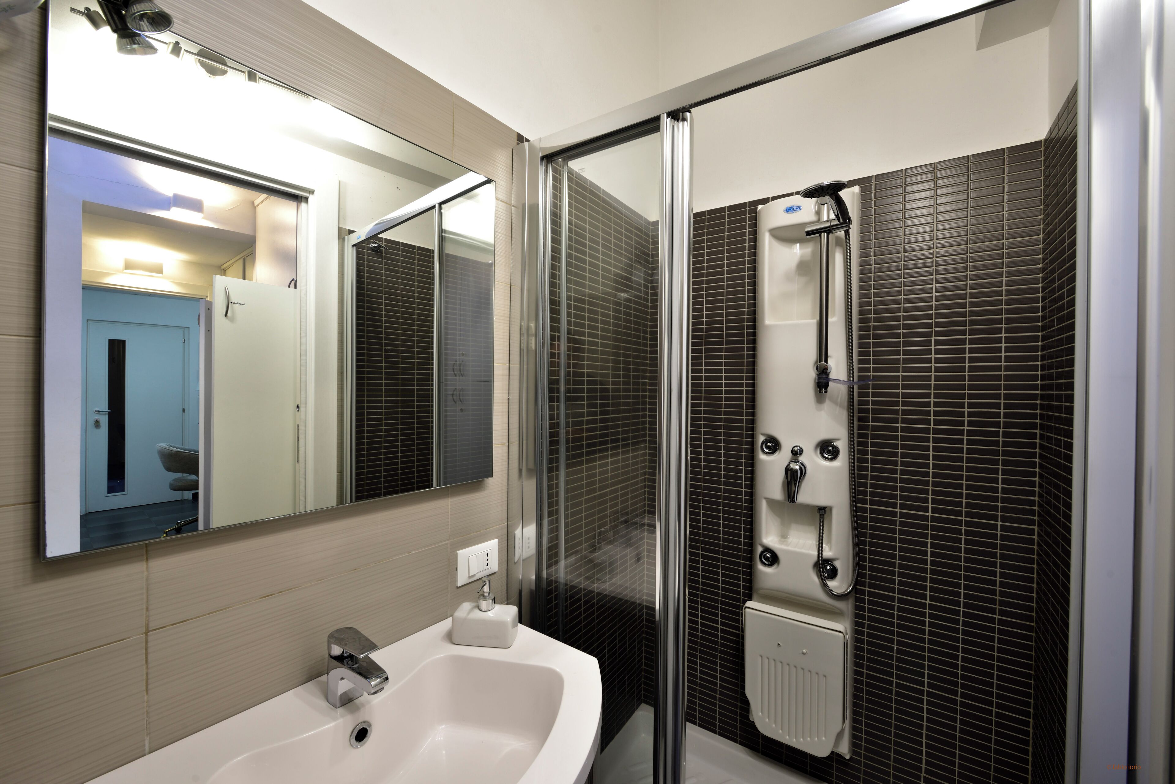 A modern bathroom with a white sink, a large mirror, and a glass-enclosed shower area.