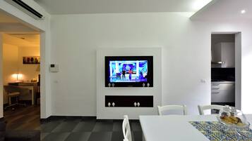Un espace repas moderne avec un téléviseur fixé au mur, une table blanche et un chemin de table à motifs.