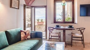 Un salon chaleureux avec un canapé vert, une table à manger avec des chaises et une grande fenêtre donnant sur l’extérieur.
