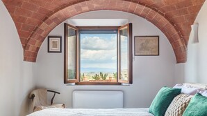 Une chambre avec un grand lit, une vue dégagée par une fenêtre ouverte et une arche en briques au-dessus de la fenêtre.