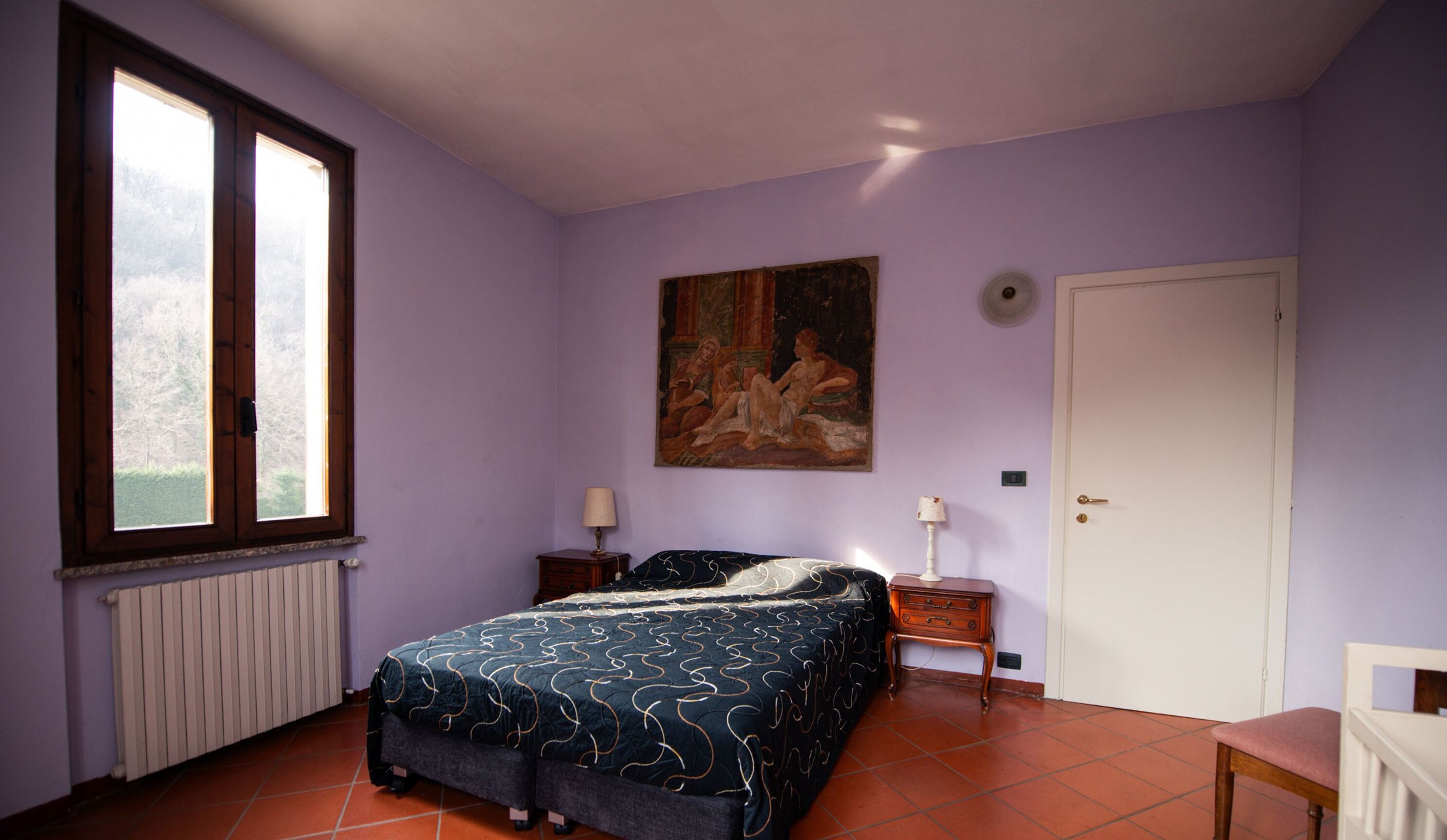 Une chambre à coucher avec un lit, une fenêtre, un radiateur, un tableau, une porte et une chaise.