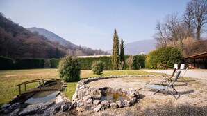 A rustic outdoor setting with a stone bridge, a circular stone structure, and a wooden deck with chairs. - Villa Catharina in Ro Volciano (Roe Volciano)