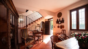 A traditional interior with a wooden staircase, a dining area with a table and chairs, and a wall-mounted shelf with kitchen utensils. - Villa Catharina in Ro Volciano (Roe Volciano)