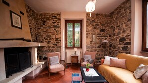 A cozy living room with a stone wall, a fireplace, a sofa, a coffee table, and a television. - Villa Catharina in Ro Volciano (Roe Volciano)