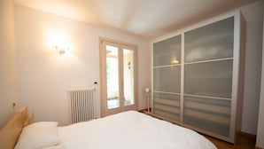 Ein Schlafzimmer mit einem Bett, einem Heizkörper, einem Kleiderschrank mit satinierten Glastüren und einer Tür zu einem Außenbereich.