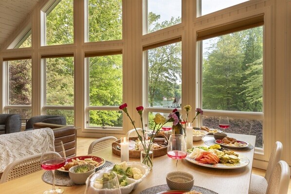 A dining area with a table set for a meal, large windows, and a view of trees.