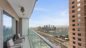 Un balcon doté d’une balustrade en verre, offrant une vue sur un paysage urbain avec de hauts immeubles et une marina.
