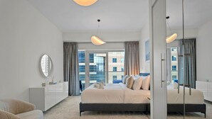 Une chambre d’hôtel moderne dotée d’un grand lit, d’un coin salon avec un canapé, d’une grande fenêtre avec des rideaux et d’un miroir.
