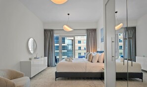 A modern hotel room with a large bed, a sitting area with a sofa, a large window with curtains, and a mirror.