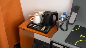 Hotelkamer met een bureau waarop een koffiezetapparaat, een waterfles, een telefoon en een laptop staan.