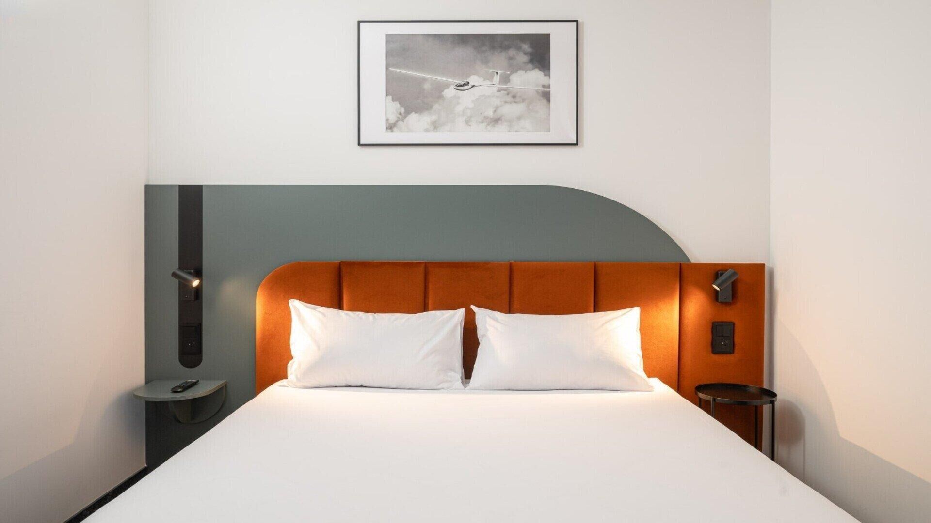 A neatly made bed with white linens and a curved headboard in a modern hotel room.