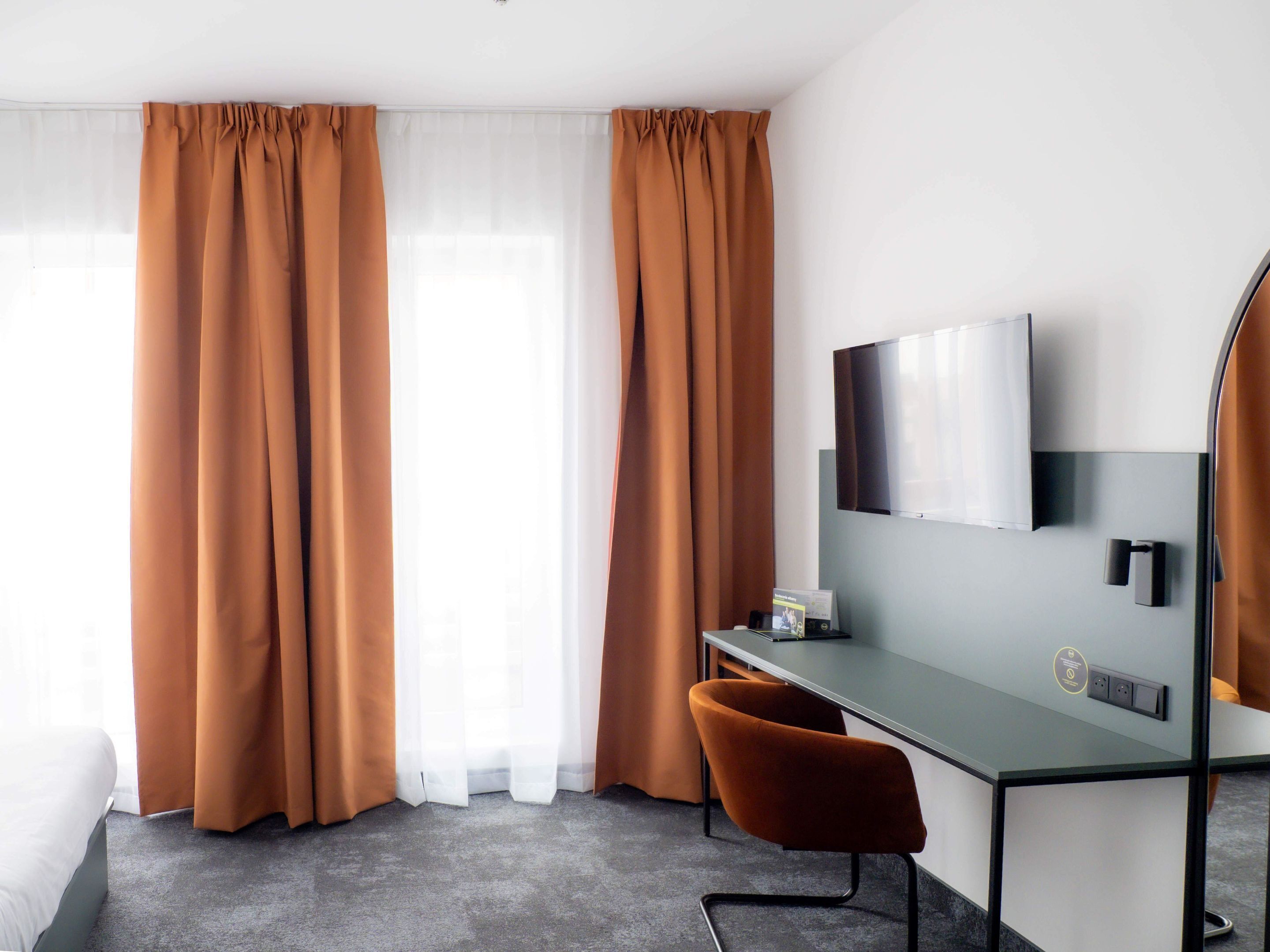 A modern hotel room with a desk, chair, and a large flat-screen TV mounted on the wall.