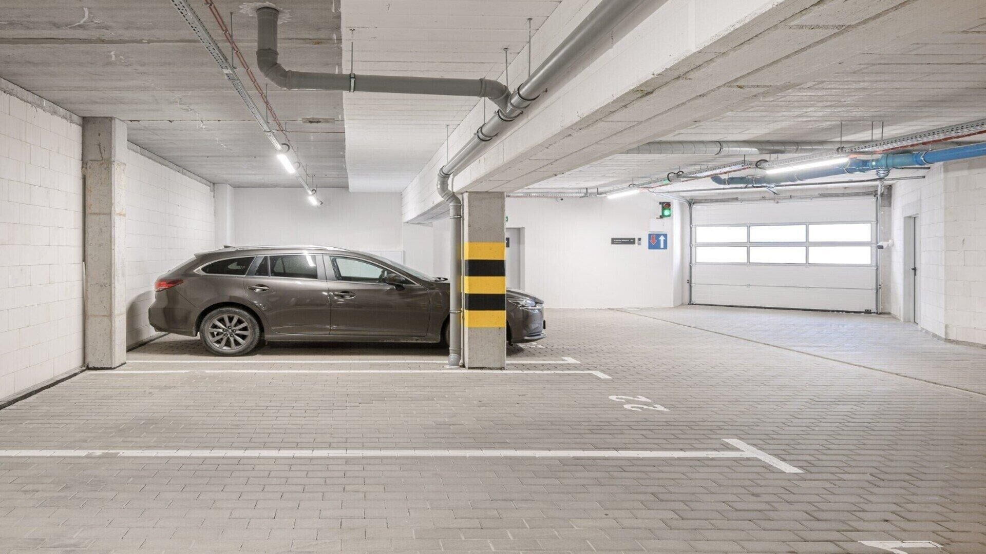 A parking garage with a car parked in a designated spot, concrete pillars, and a garage door.