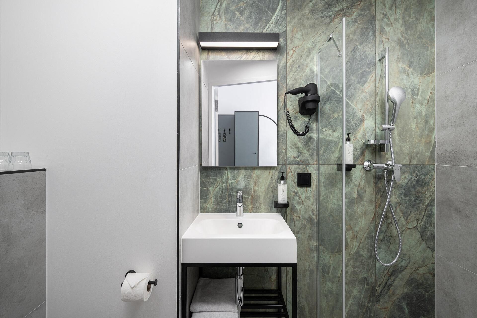 Une salle de bain moderne avec un lavabo blanc, un miroir, un sèche-cheveux et une douche.