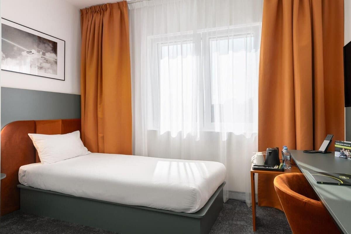 Una habitación de hotel con cama, escritorio, silla, televisor y ventana con cortinas.