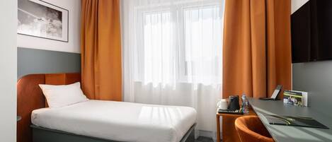 A hotel room with a bed, a desk, a chair, a television, and a window with curtains.