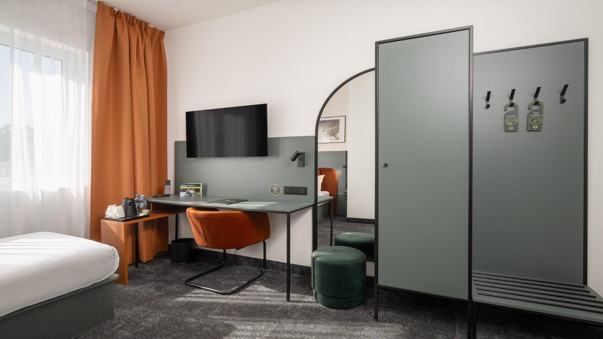 A hotel room with a bed, desk, chair, wardrobe, and a TV.
