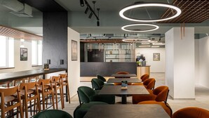 Een moderne eetruimte met houten en groen bekleden stoelen, een lange tafel en ronde plafondlampen.