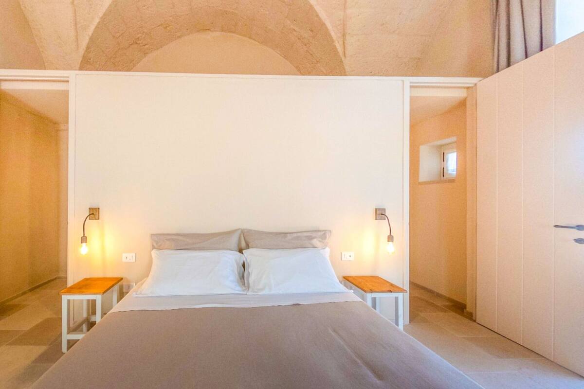 A bedroom with a large bed, two bedside tables, and two wall-mounted lamps.