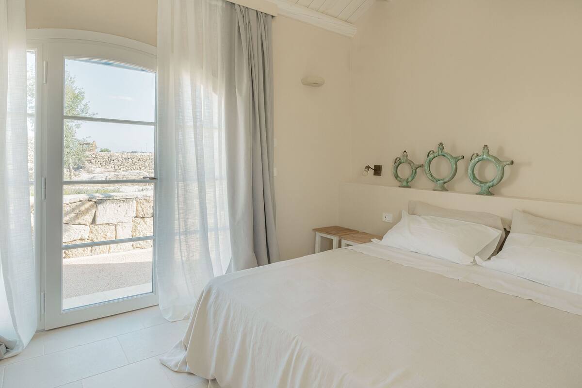 A bedroom with a large bed, a nightstand, and a window with curtains.