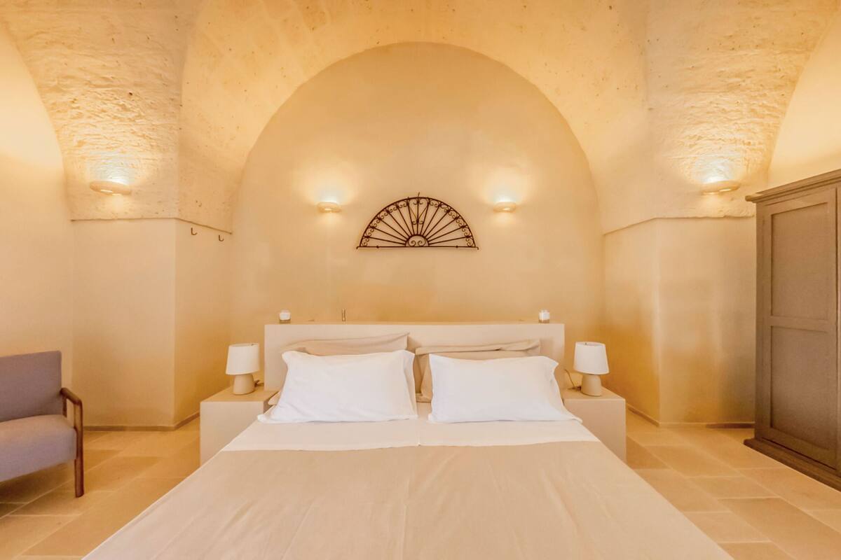 A bedroom with a large bed, two bedside tables with lamps, a sofa, and a wardrobe.