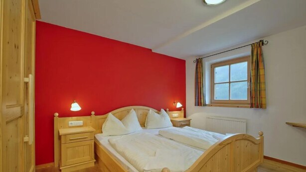 A bedroom with a wooden bed, two bedside tables, a window with curtains, and a red wall. - Scenic Valley Chalet in Austria (Wald im Pinzgau)